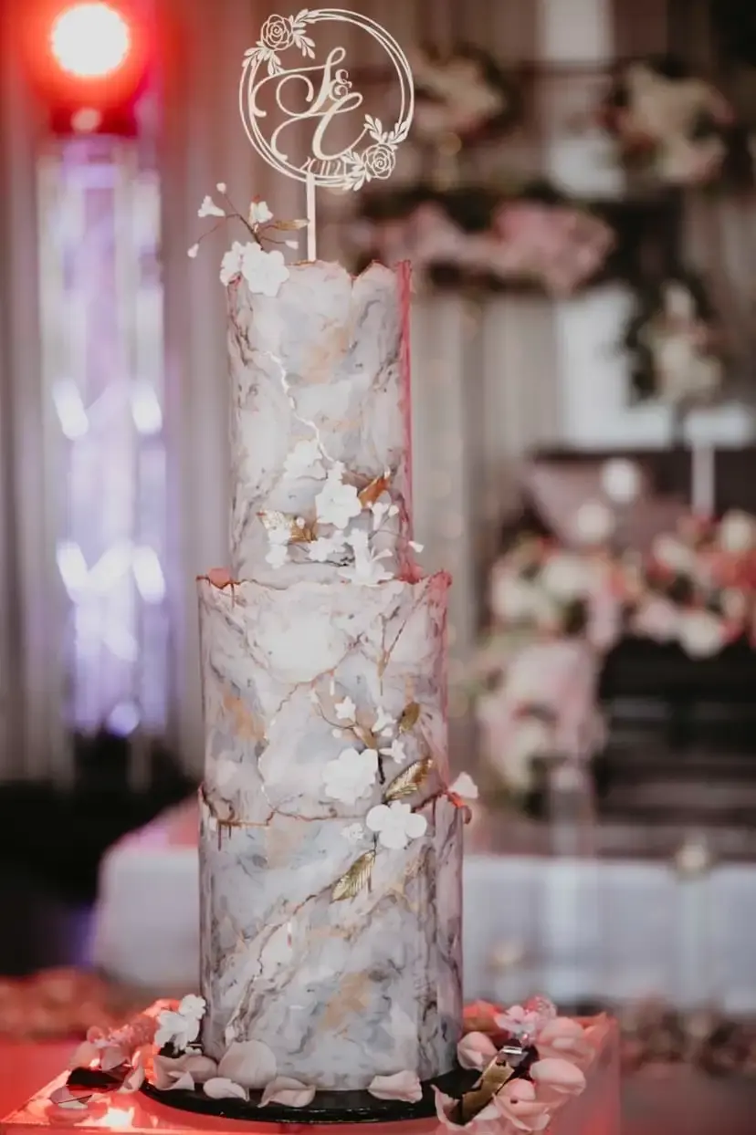Tall two-tier wedding cake with marble icing, gold leaf detailing and white sugar flowers
