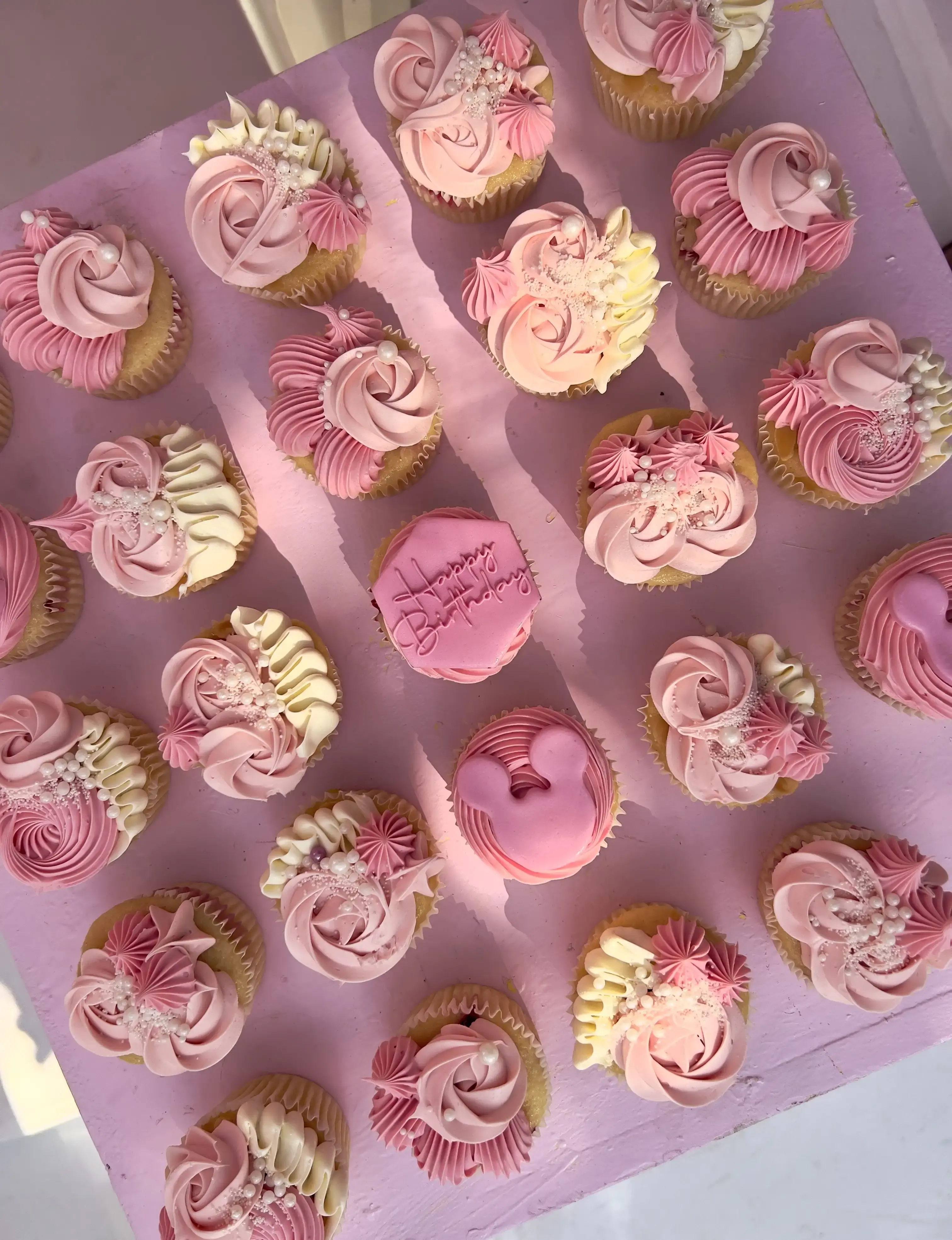 Overhead flatlay of pink and cream rosette-piped cupcakes with a Minnie Mouse silhouette plaque