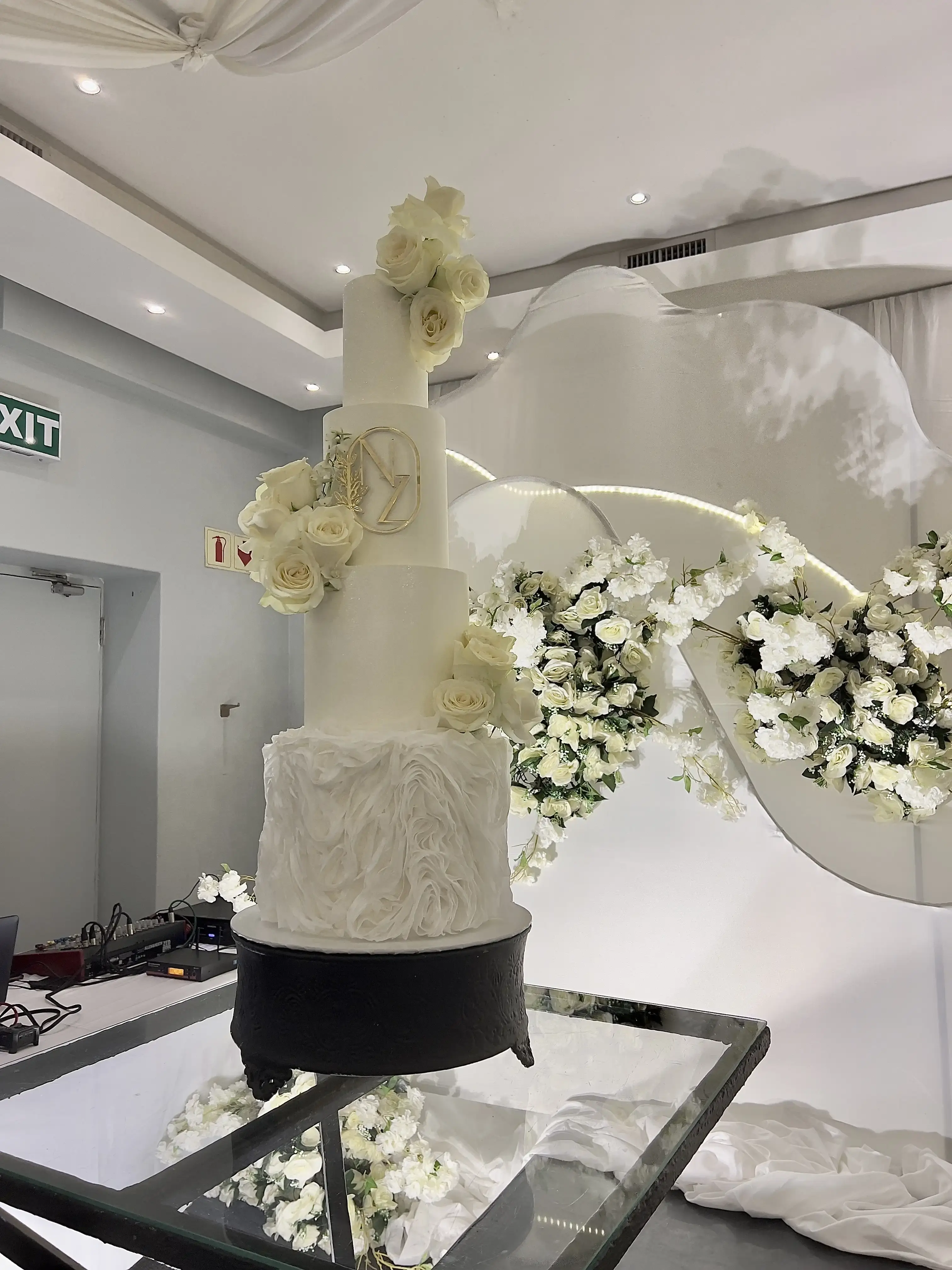 Tall wedding cake with a ruffled fondant base tier, white roses and a gold circular monogram