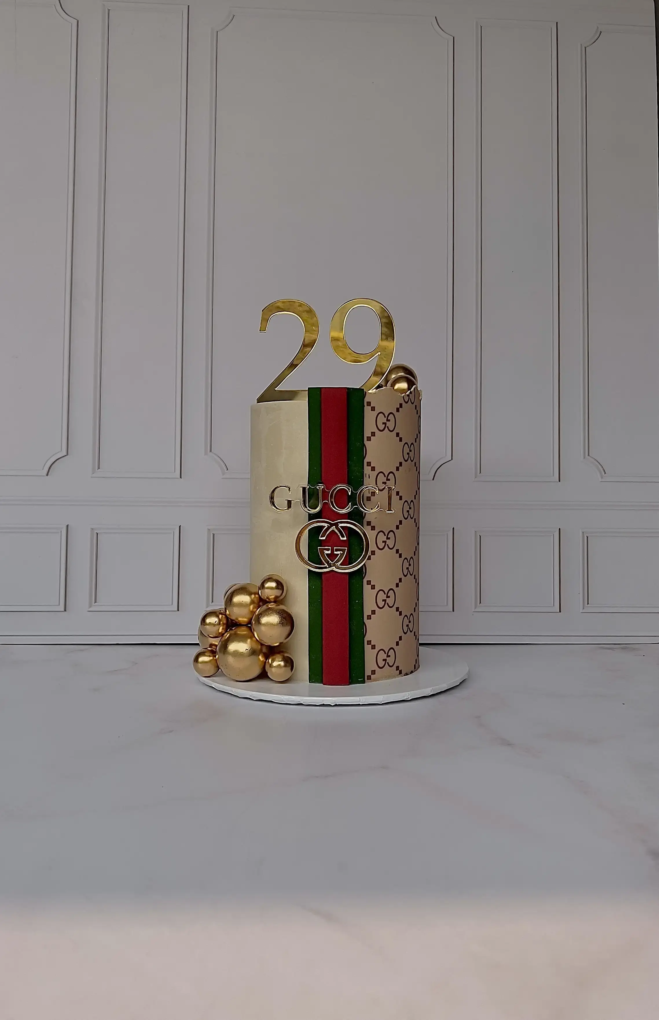 Cream cake wrapped in a designer-inspired striped and monogram pattern with gold spheres