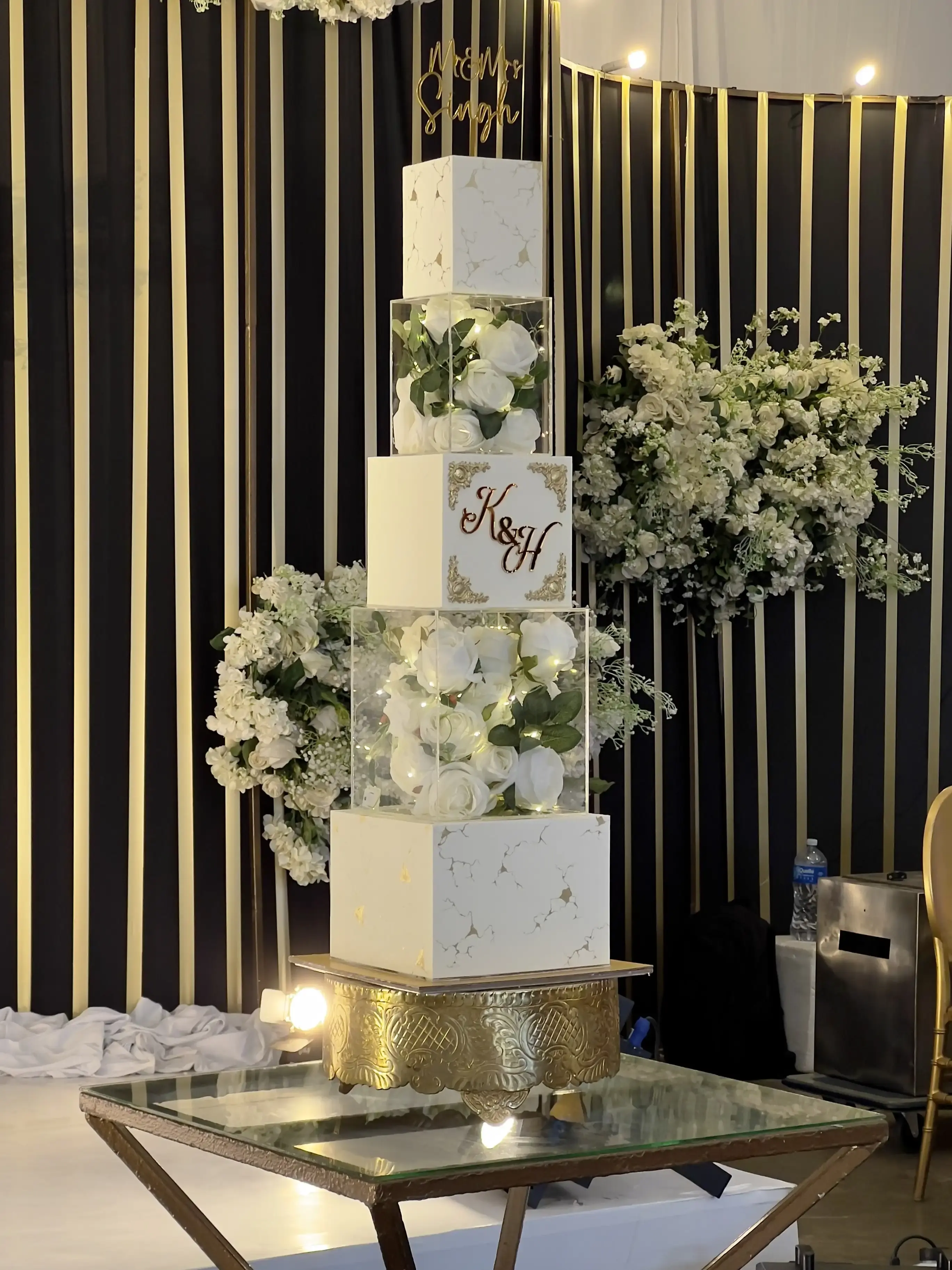 Wedding cake with square fondant tiers and acrylic cubes of fresh roses and fairy lights, gold “Mr & Mrs” topper