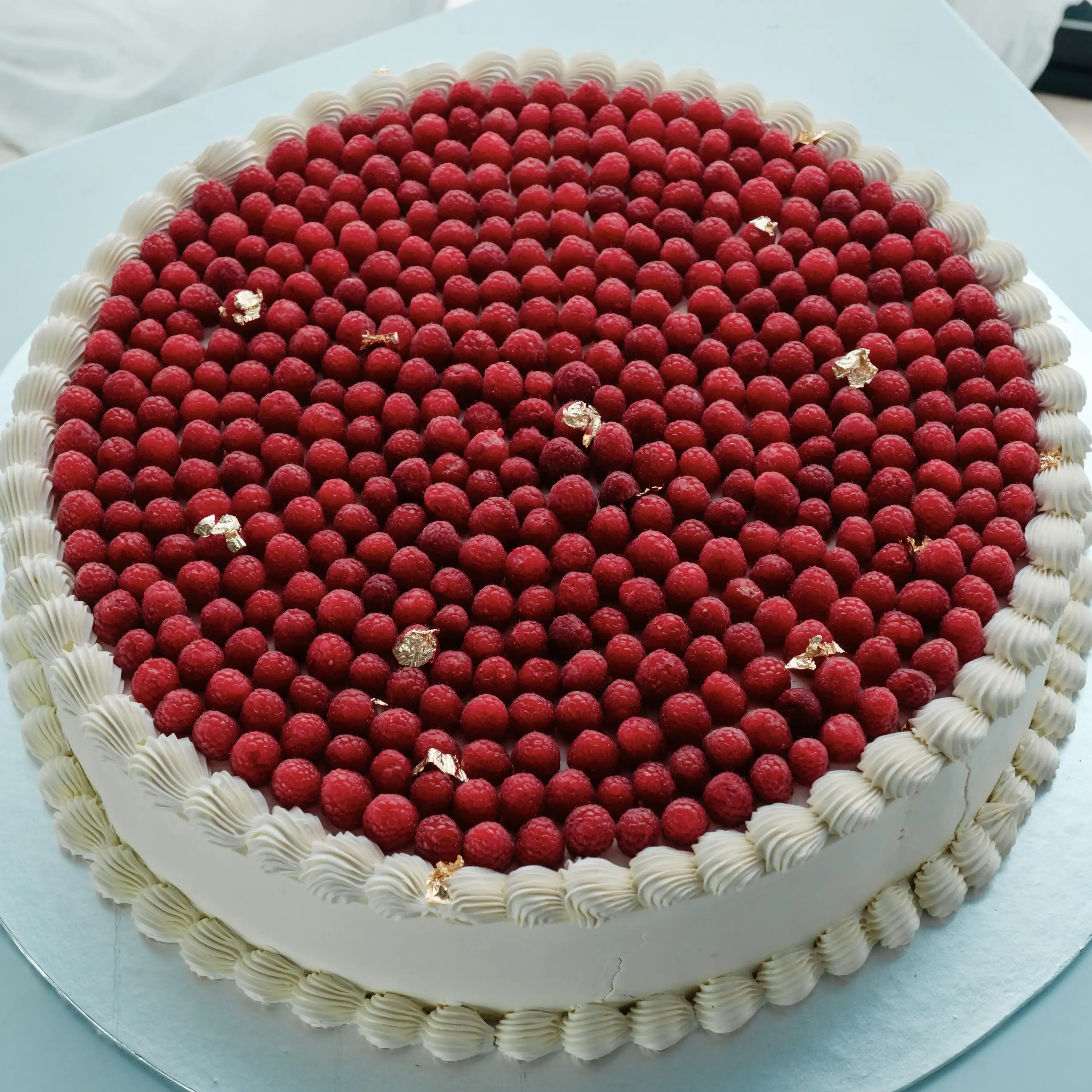 Round cake topped edge-to-edge with fresh raspberries and flecks of gold leaf