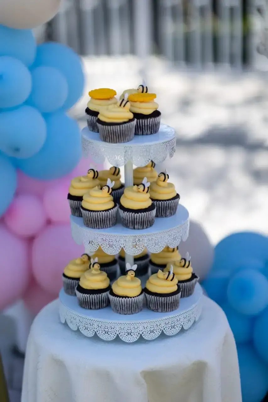 Three-tier lace-edged stand of chocolate cupcakes topped with cream swirls and fondant bees