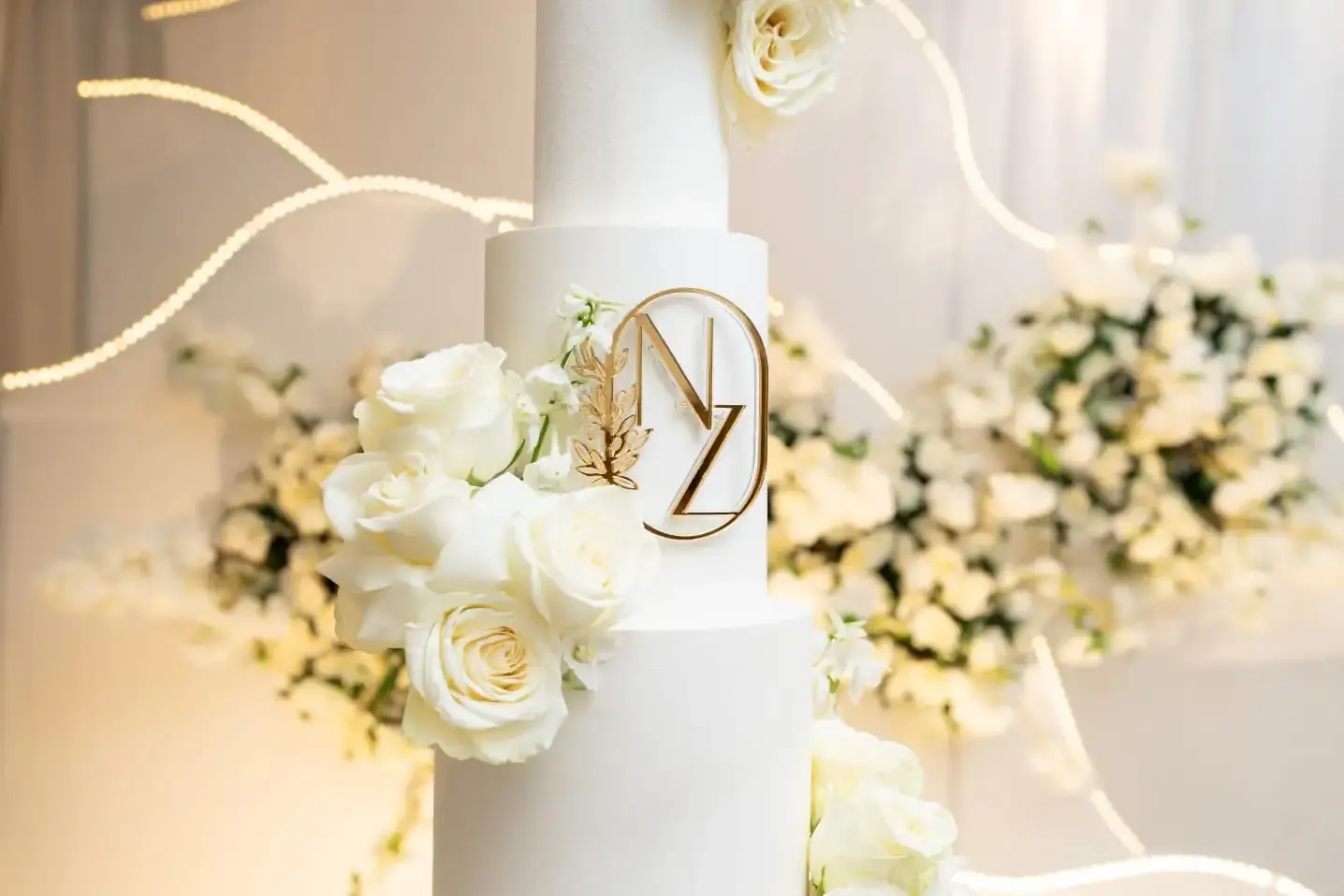 Detail of a gold circular monogram and white roses on a ruffled-base wedding cake