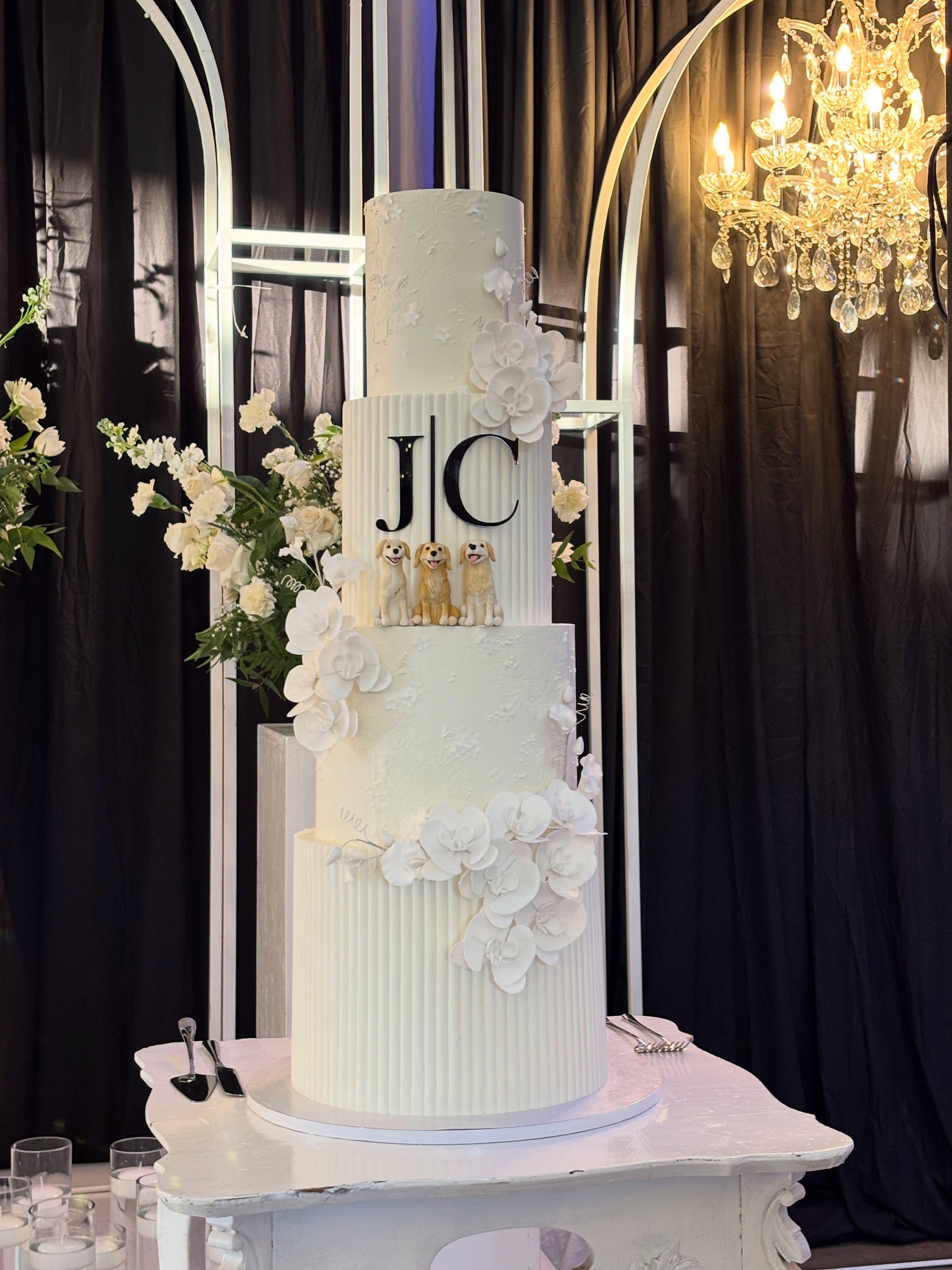 Four-tier white wedding cake with a monogram, sugar orchids, and dog toppers